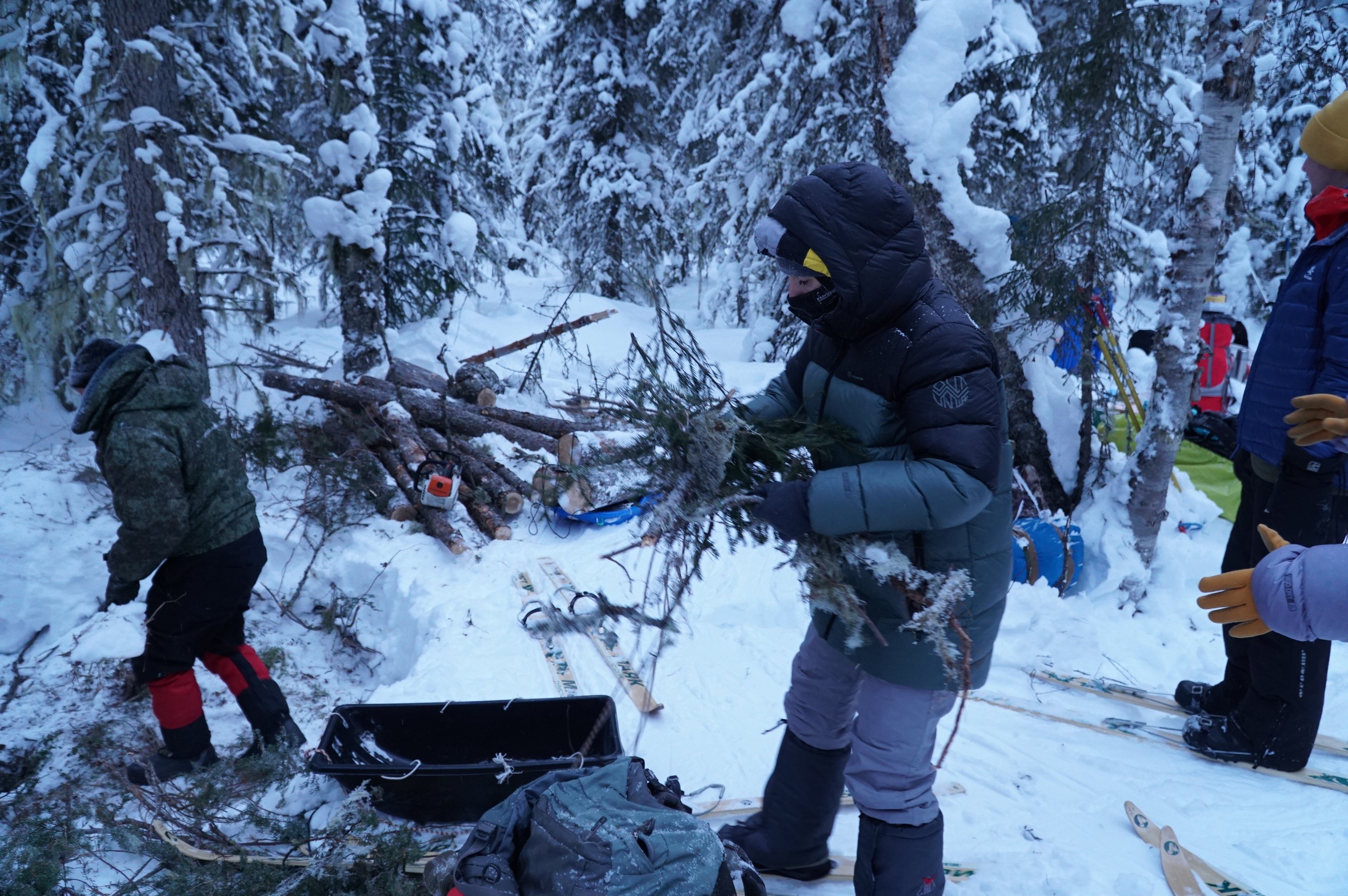 pessoas a recolher lenha e equipamento numa floresta nevada