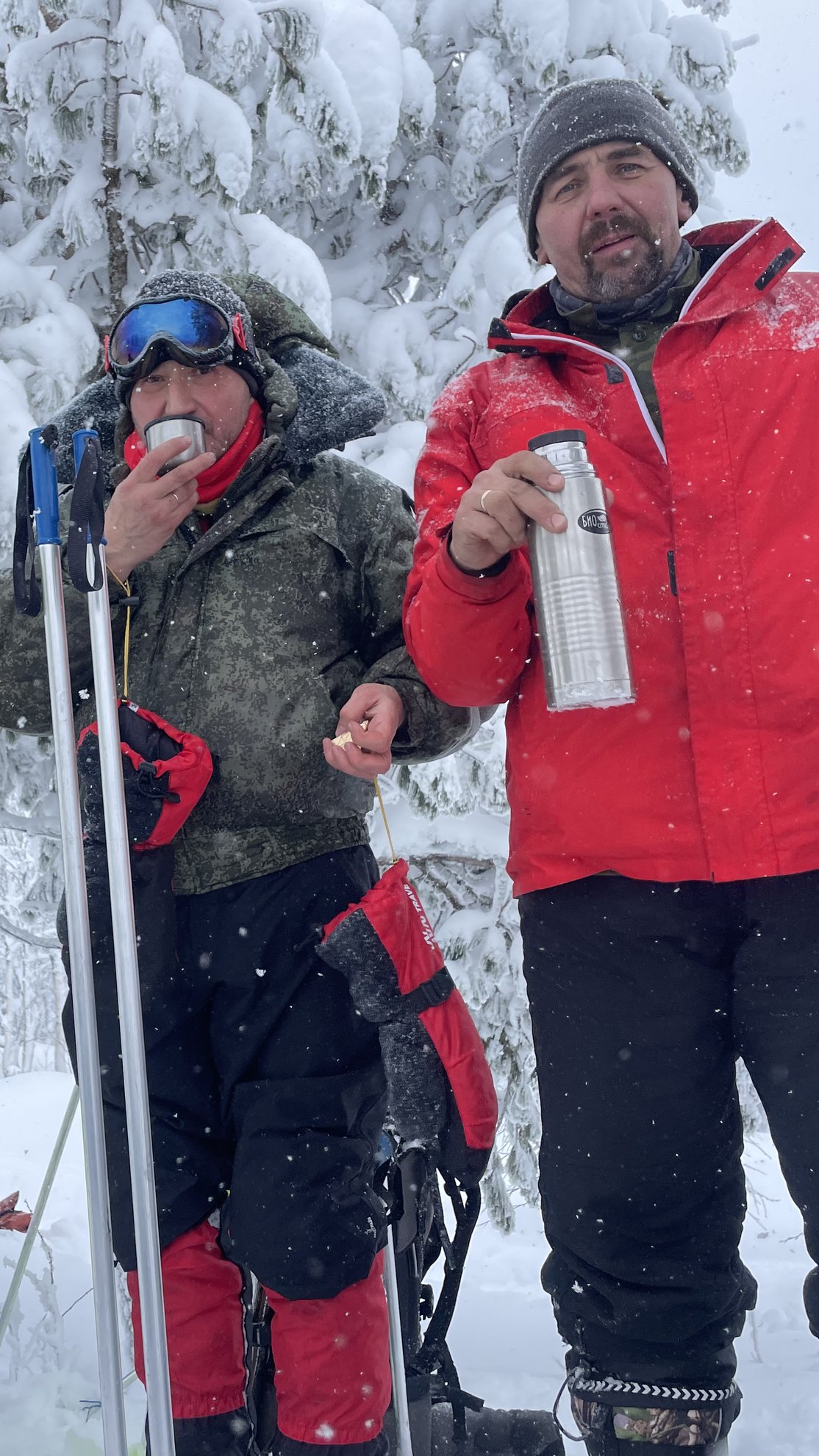 Dois homens com equipamento de inverno a segurar uma chávena e uma garrafa térmica