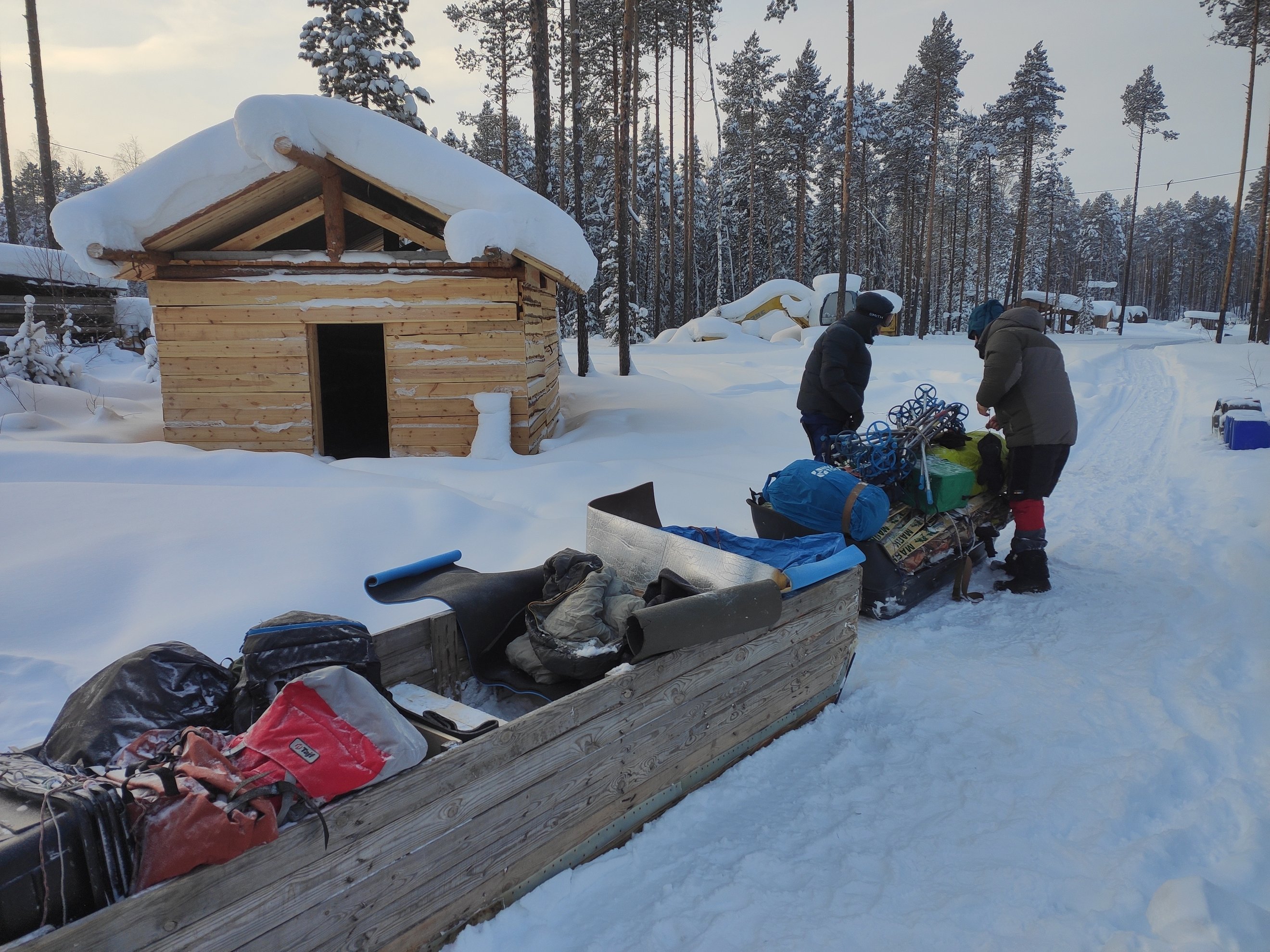 Gear and supplies loaded on sleds near a log cabin