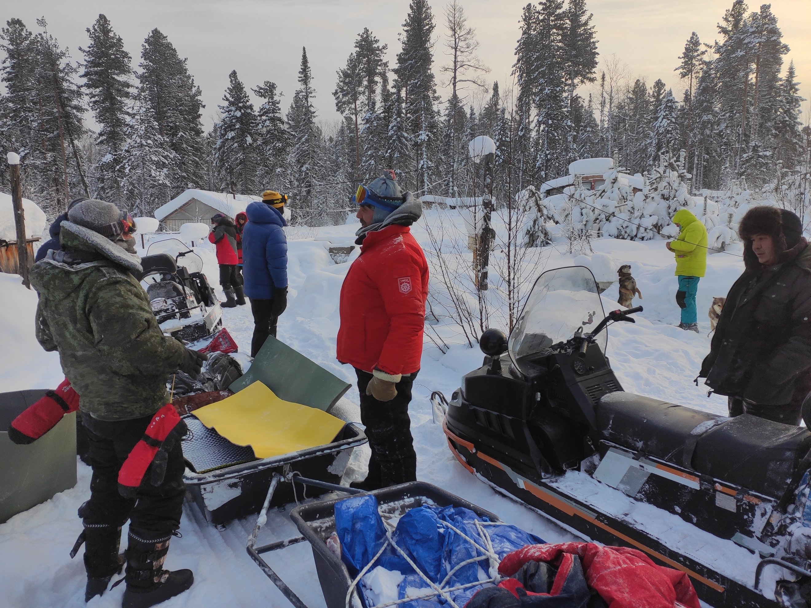 people standing near snowmobiles and gear in snow