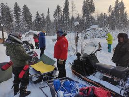 people standing near snowmobiles and gear in snow