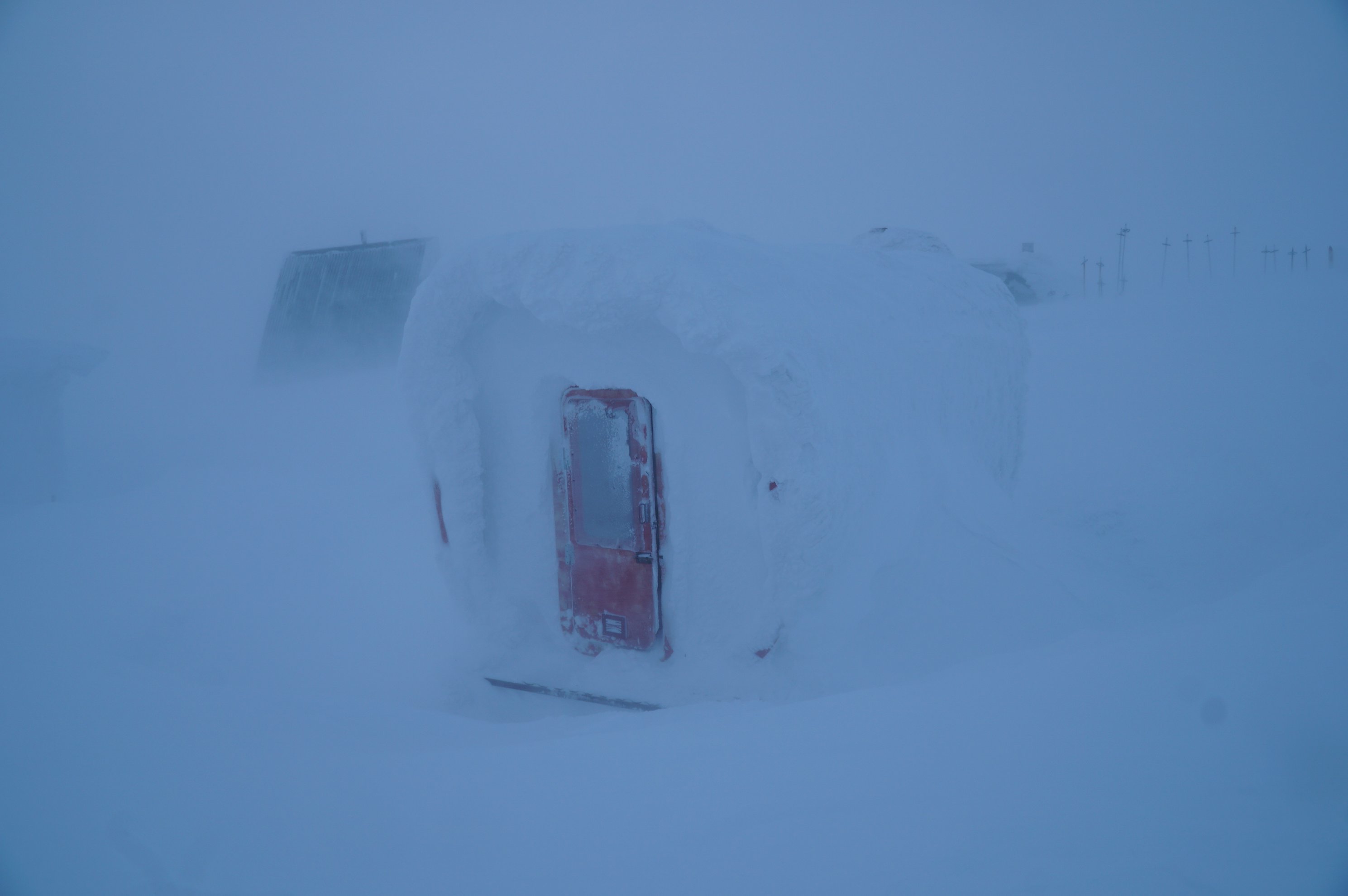 Snow-covered refuge building with red door in fog