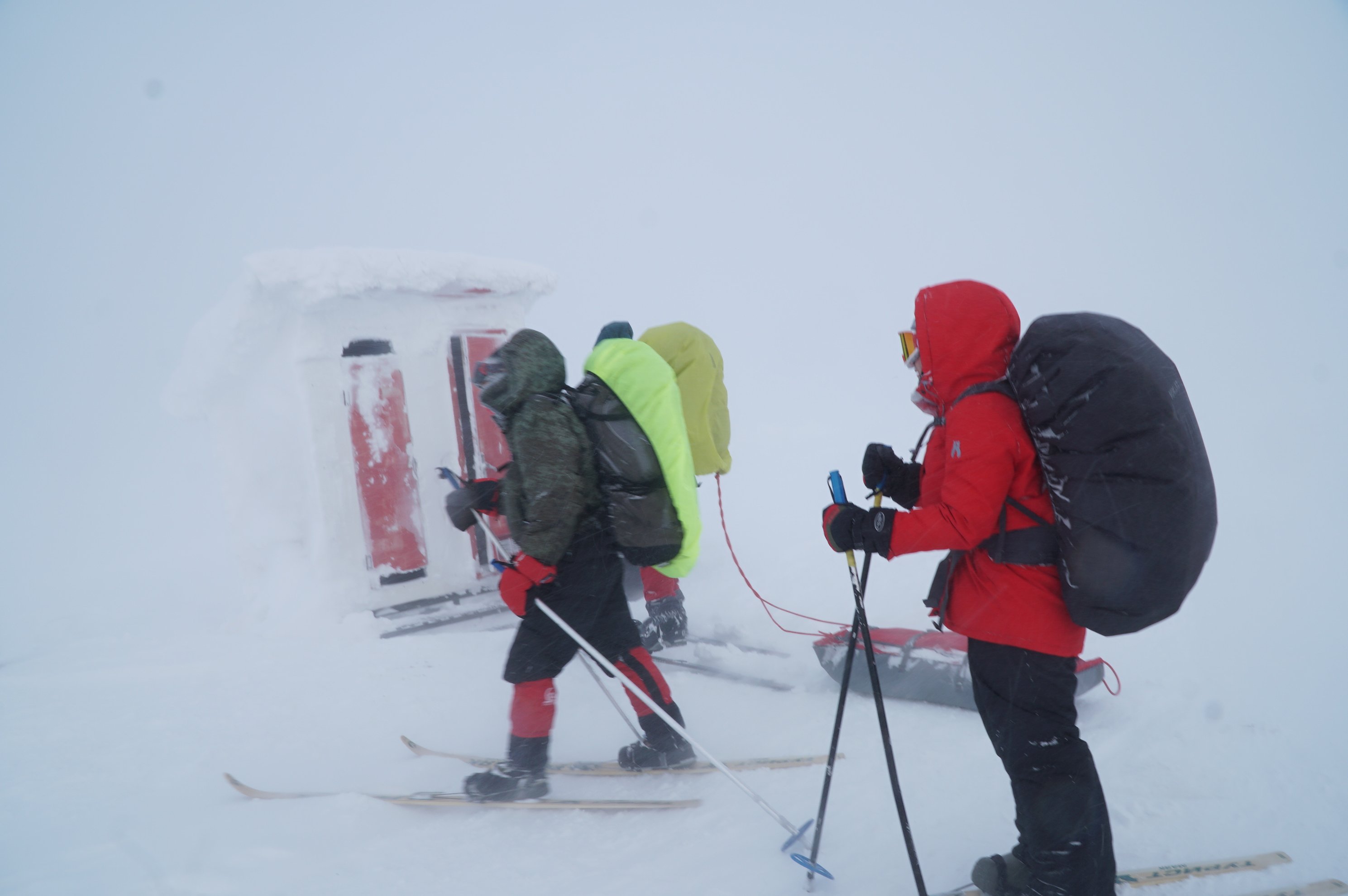 Three skiers standing next to a snow-covered wooden shelter