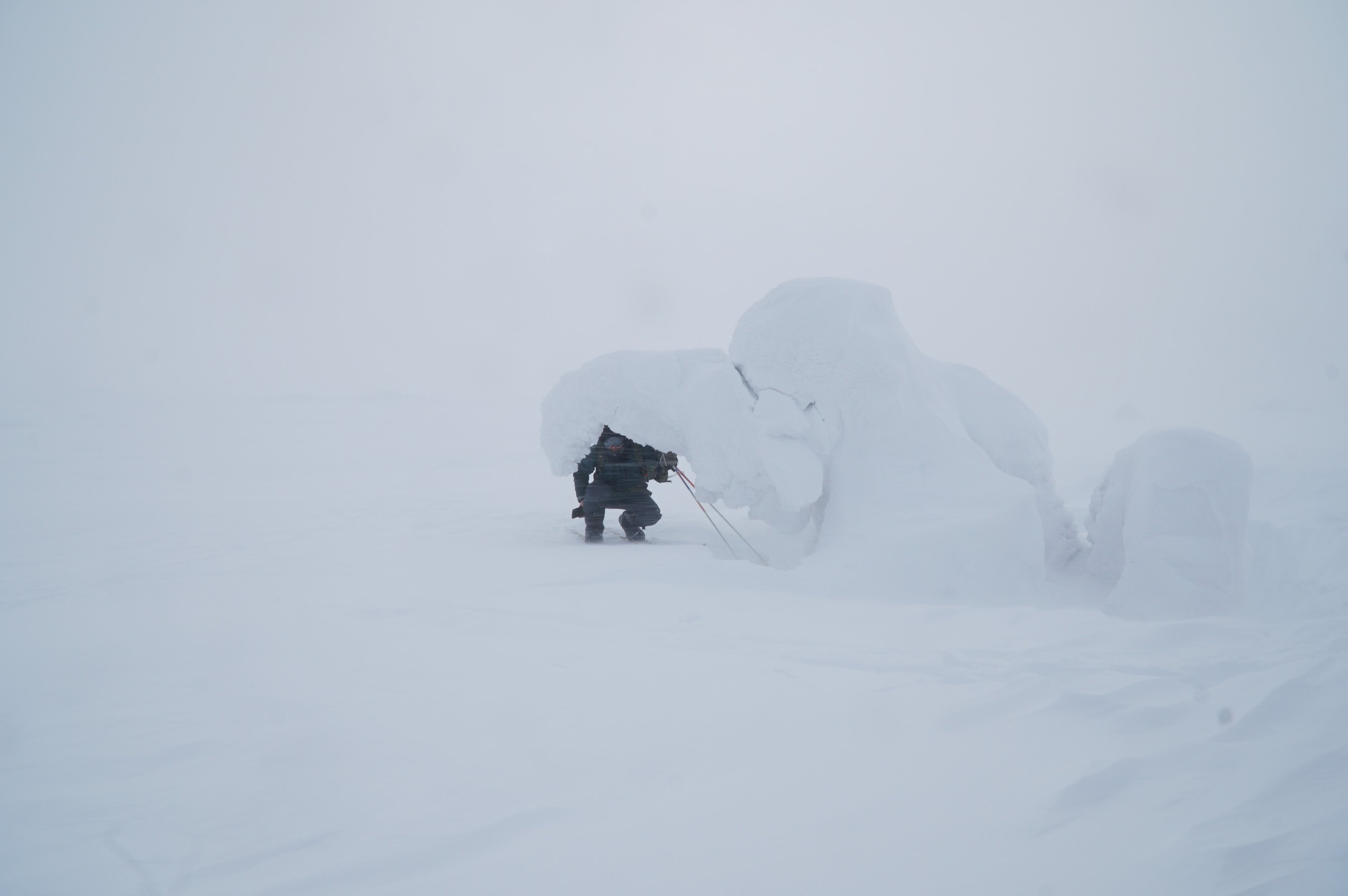 person in ski gear crouching beside a snow drift