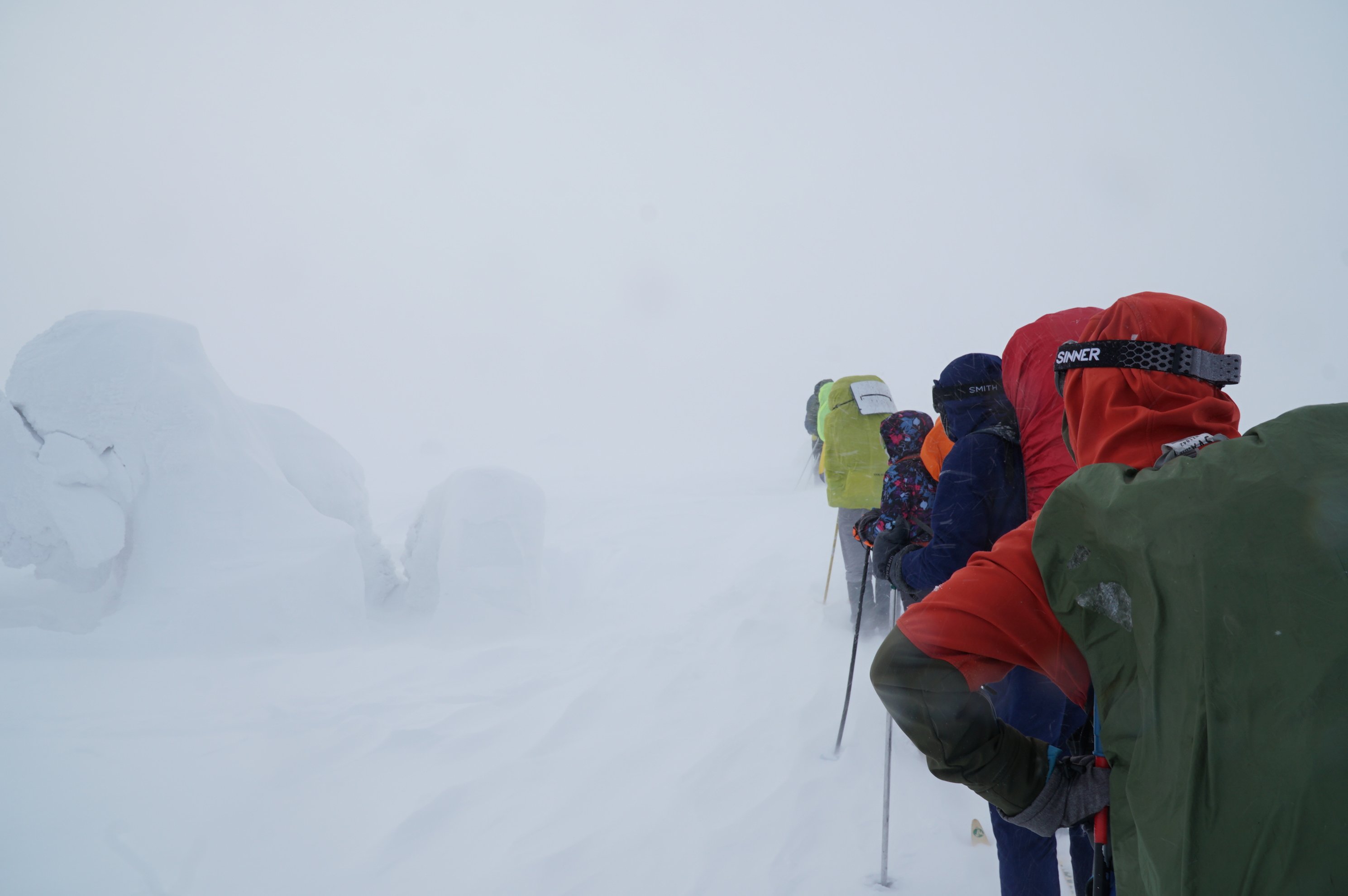 Line of skiers moving through a whiteout snowstorm