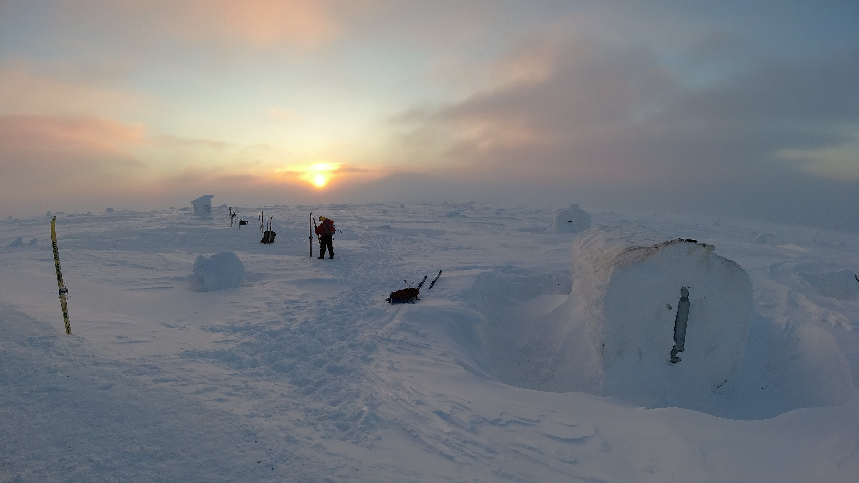 snow-covered shelters at sunset with a person standing nearby