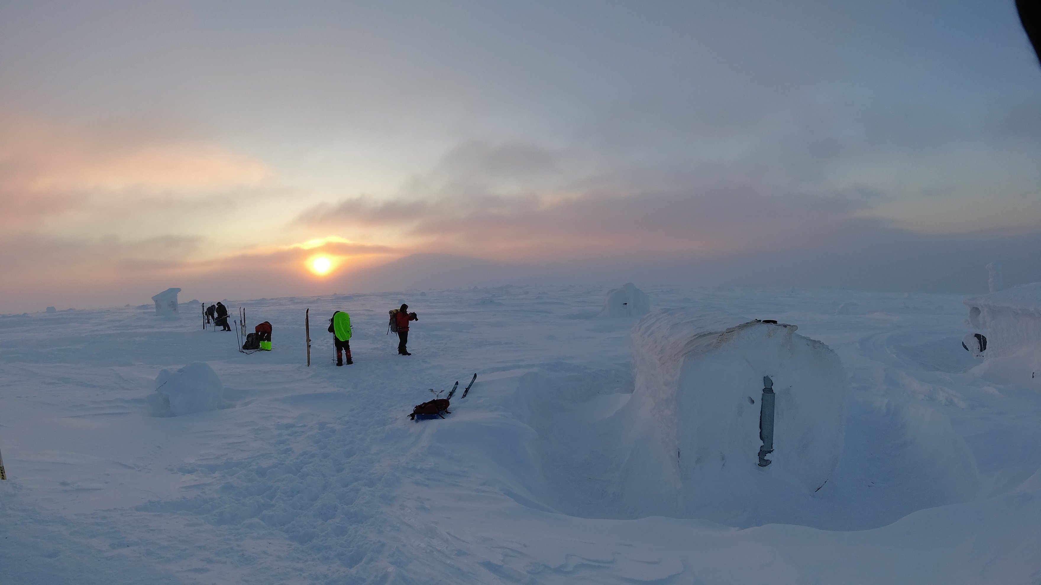 snow shelters and skiers at sunset