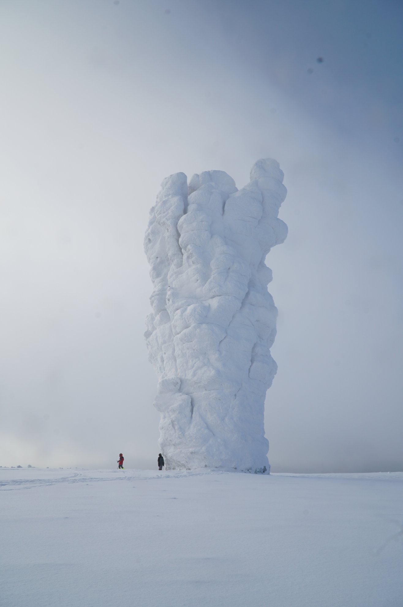snow covered rock pillar with two people standing nearby