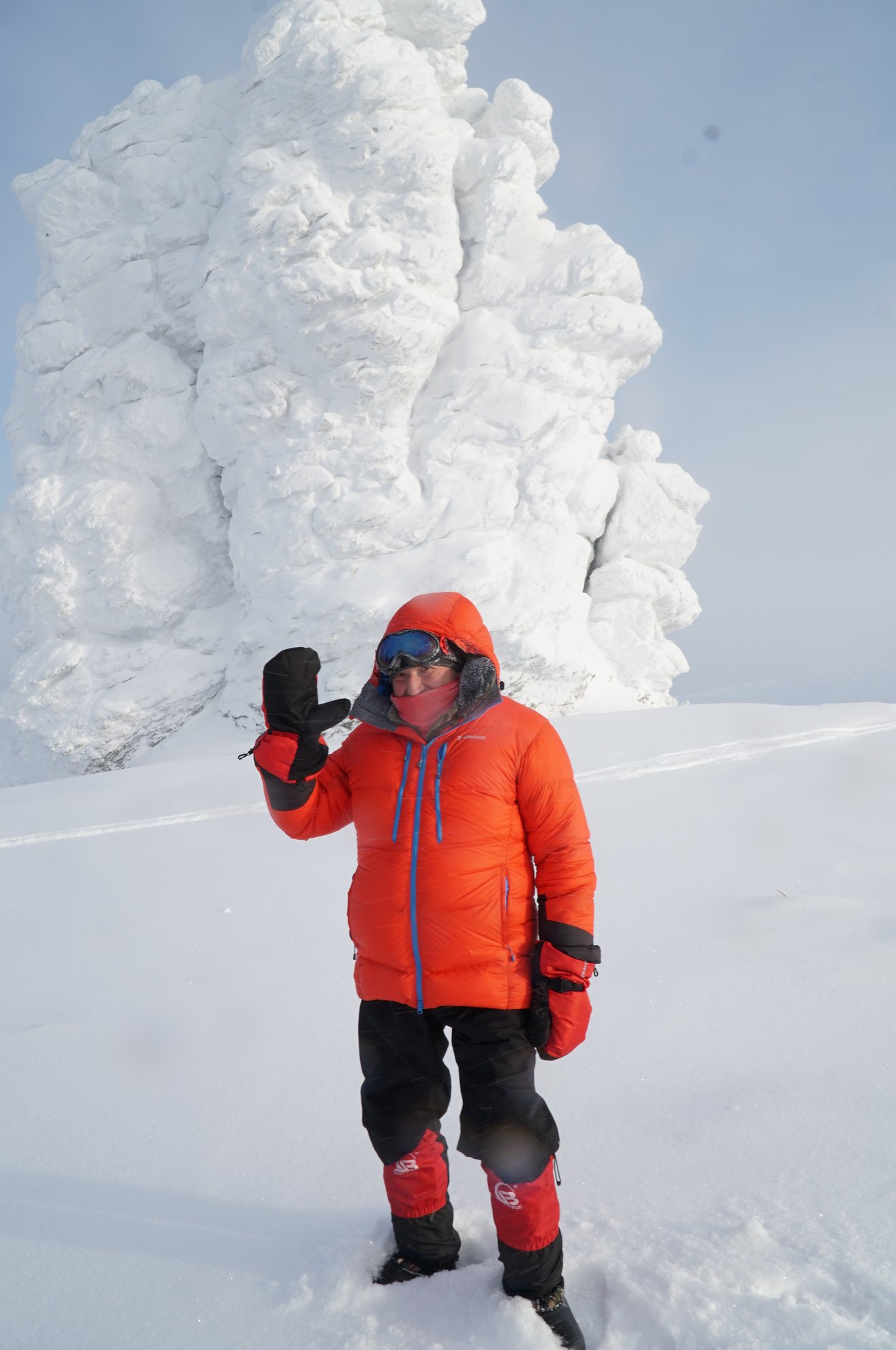 Person in orange jacket standing by snow covered rock formation