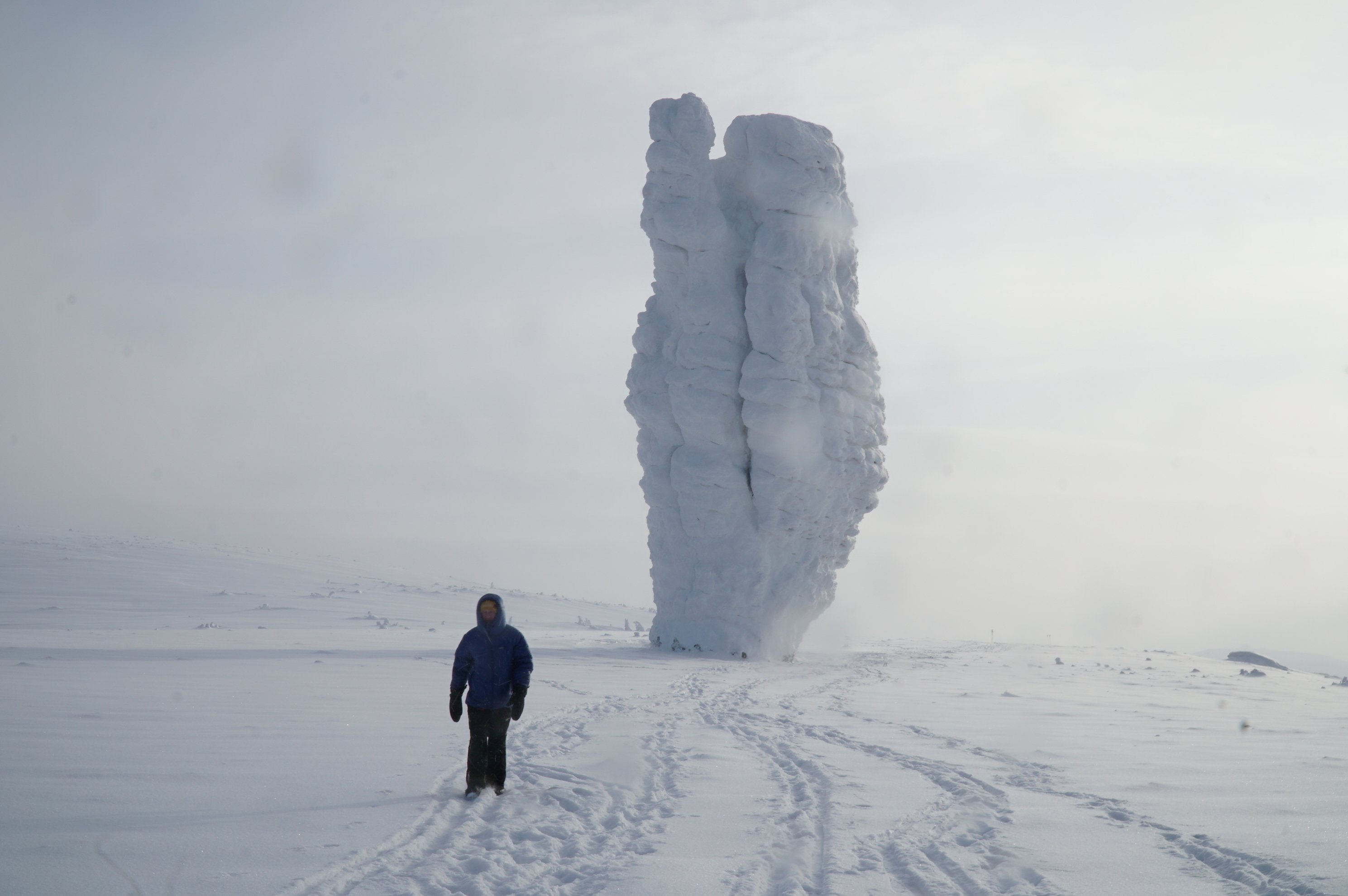 Person standing in snow beside a snow-covered rock pillar