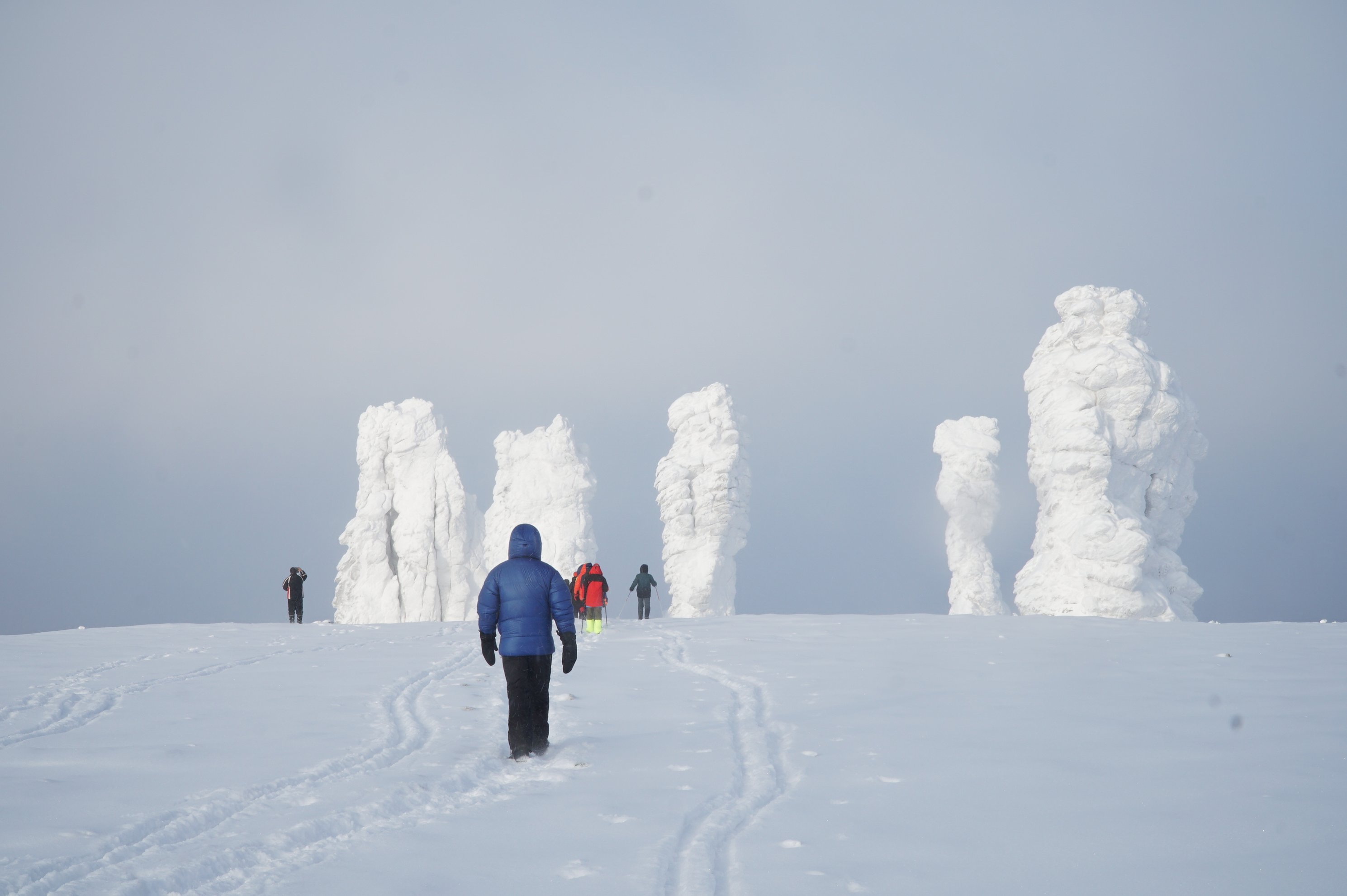 Skiers approaching snow-covered rock pillars under a grey sky