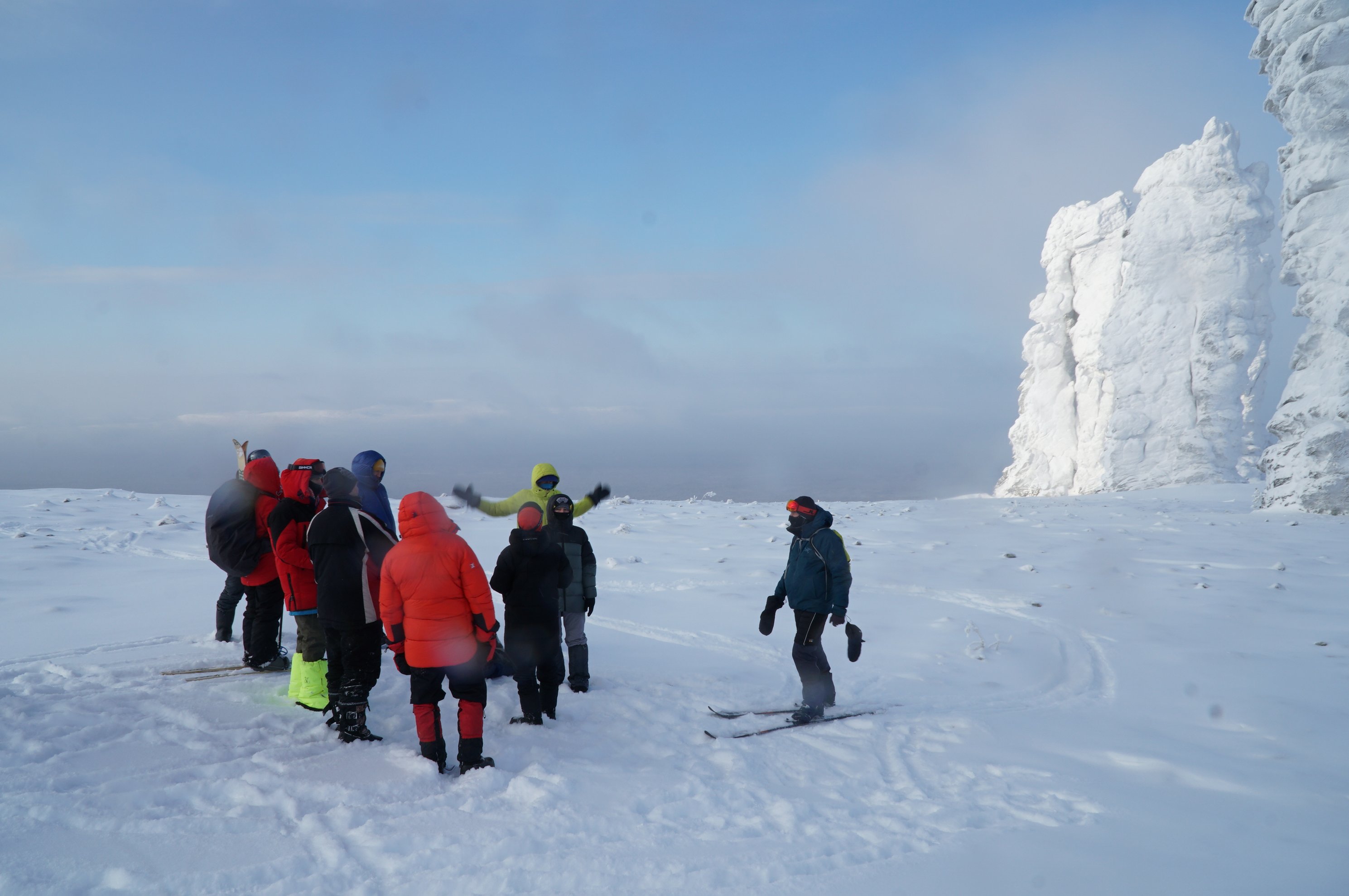 group of people on skis near a frozen rock pillar