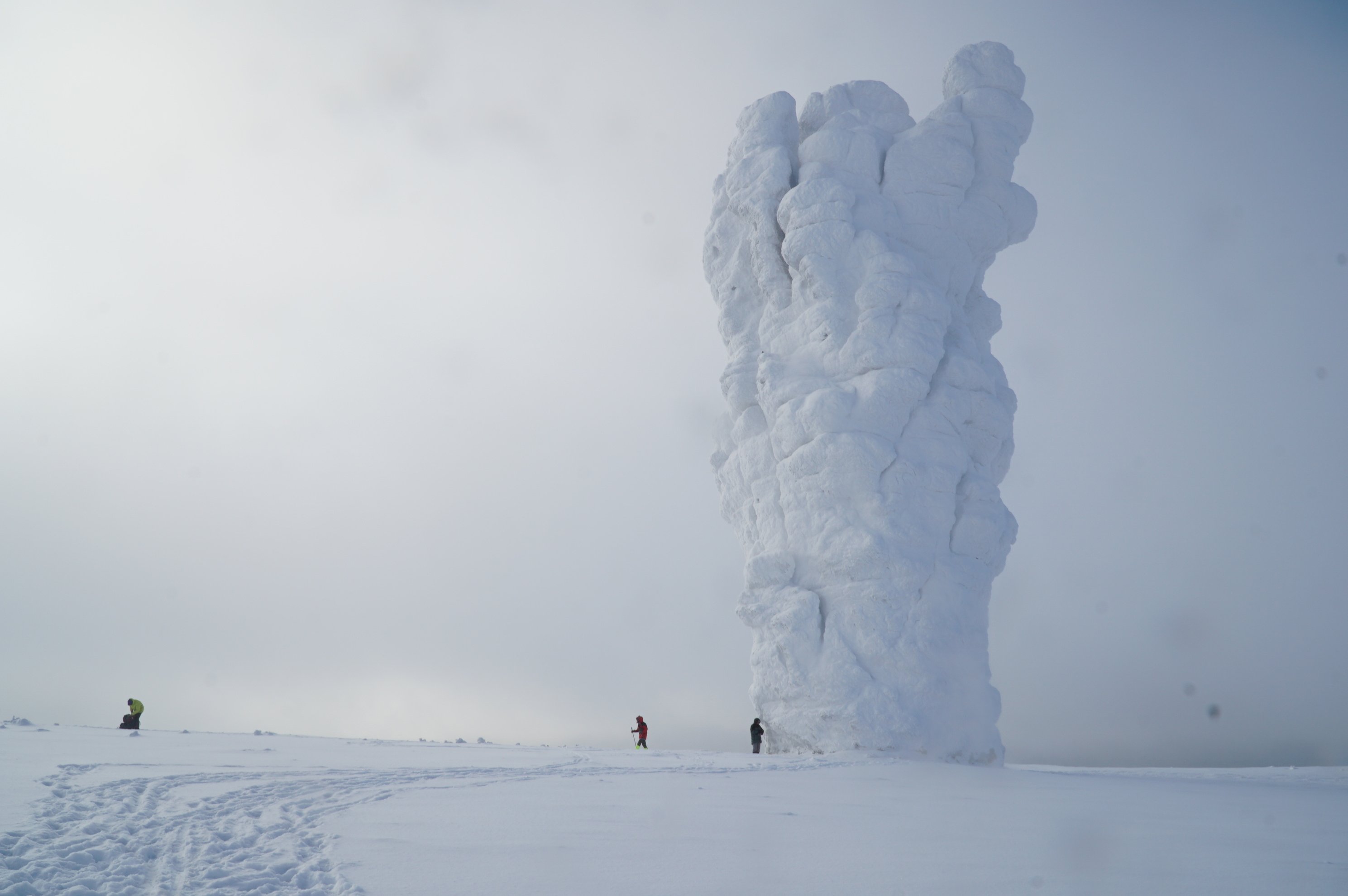 snow covered rock formation with skiers on a white plain