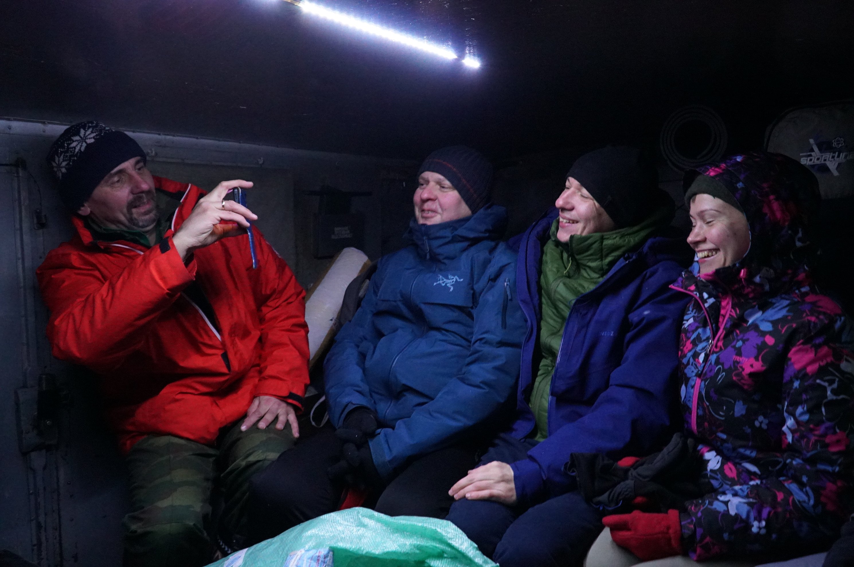 four people sitting inside a vehicle or shelter