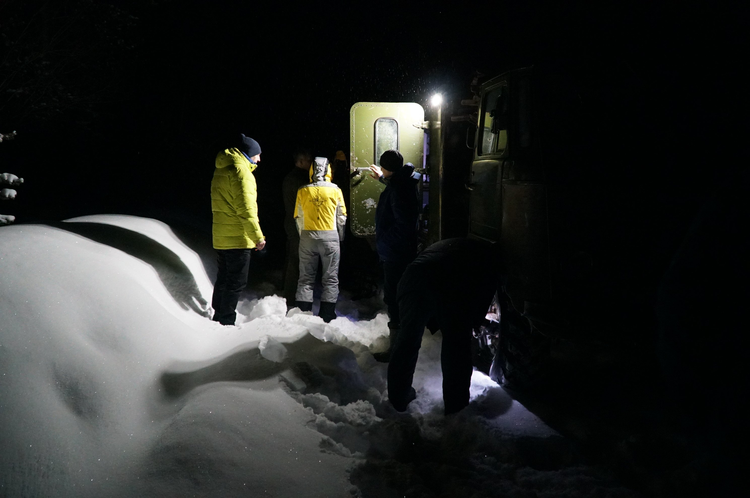 people standing by a vehicle in snow at night