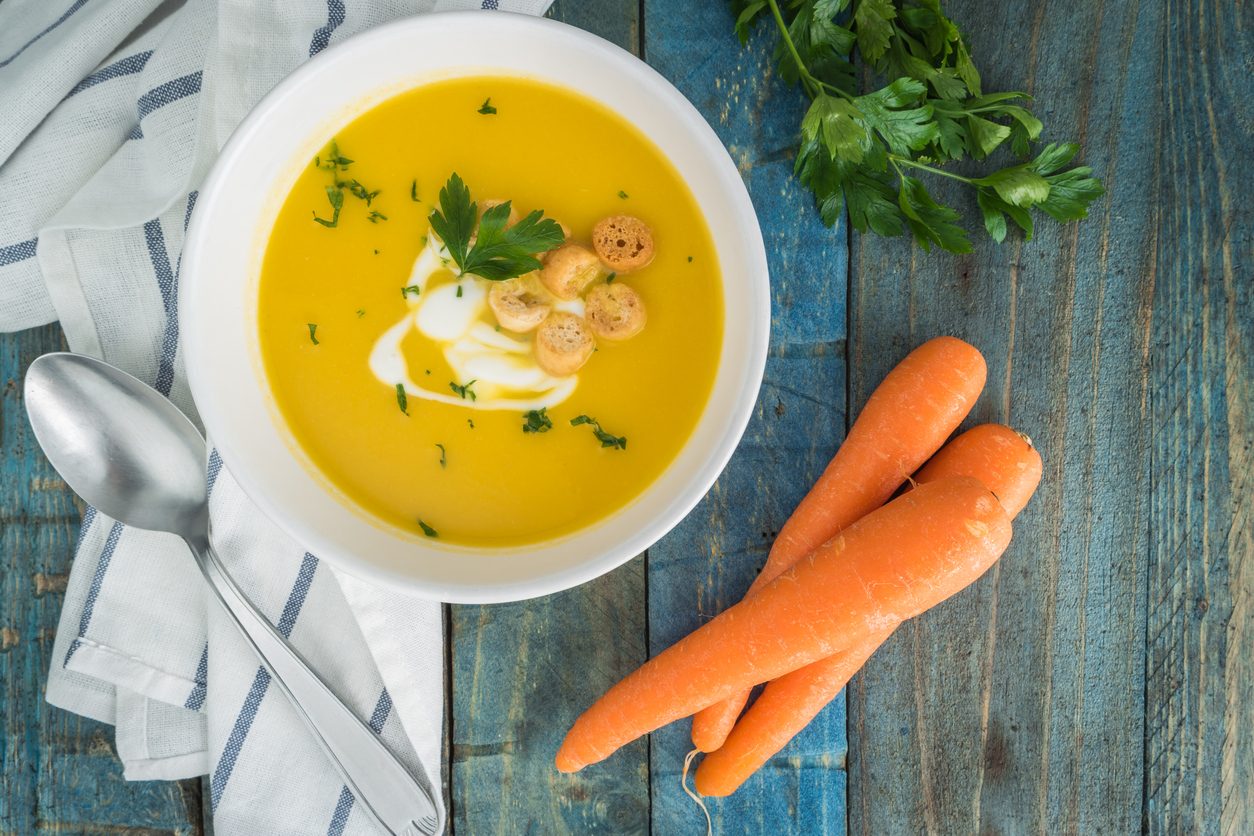 Top down view of soup bowl next to raw carrots