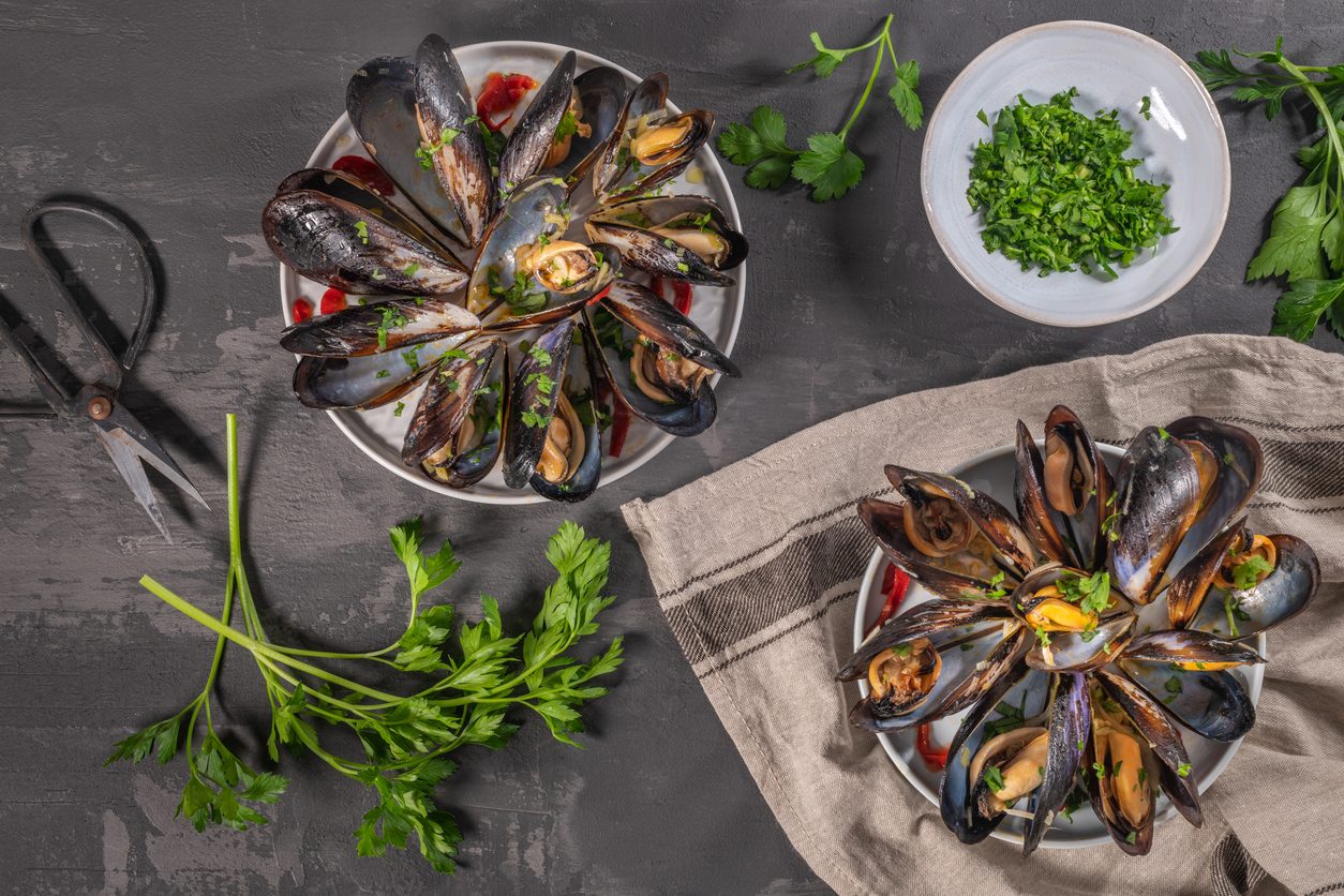 Two plates of mussels with a bowl of chopped parsley