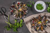 Two plates of mussels with a bowl of chopped parsley