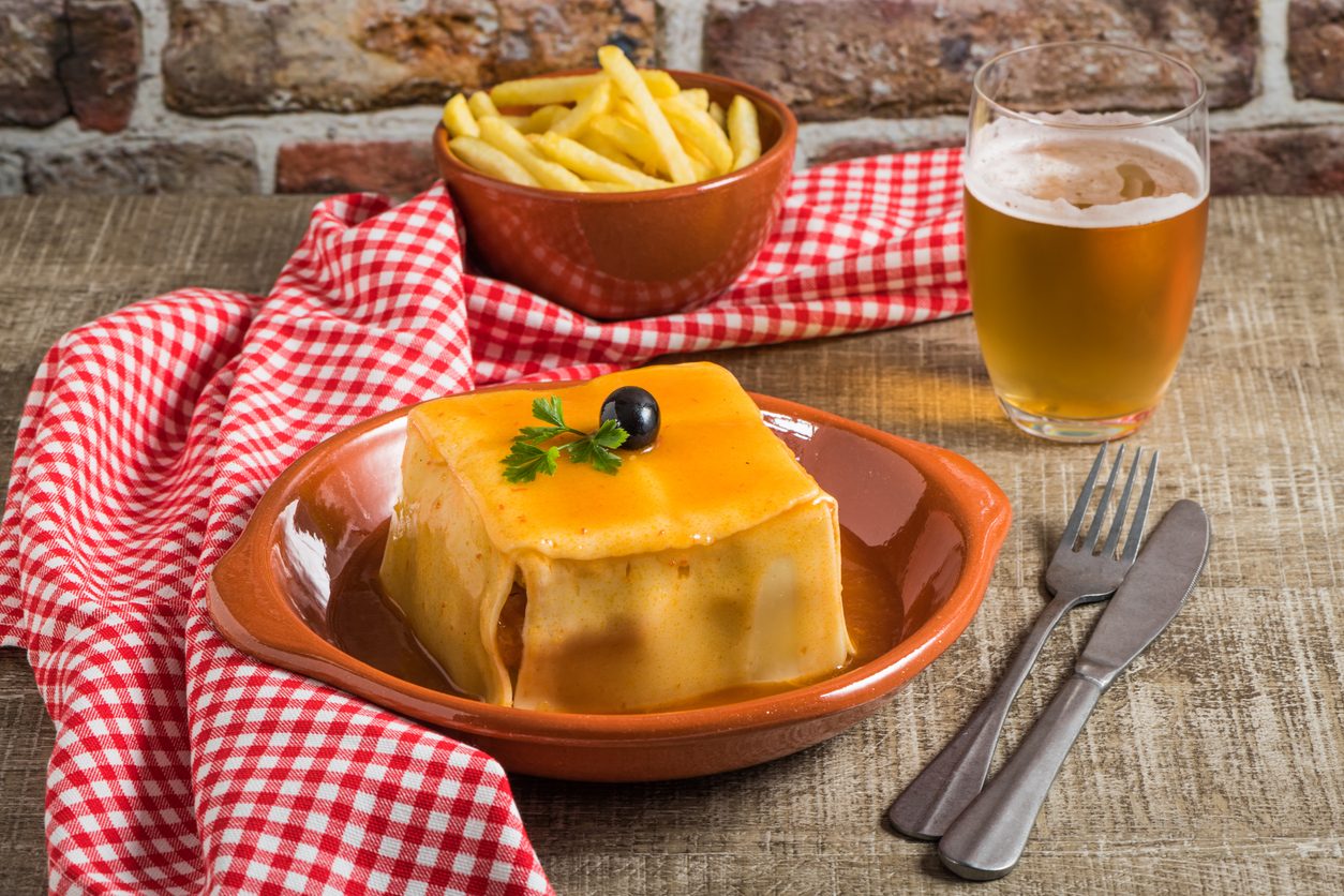 Sandwich with cheese sauce, bowl of fries, and glass of beer