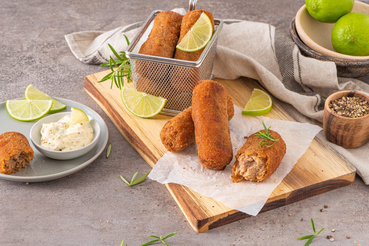 крокеты на деревянной доске с соусом и дольками лайма