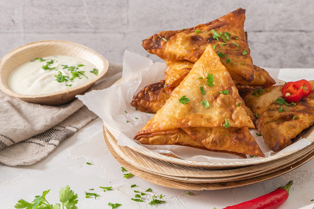 three samosas on parchment paper with a side of yoghurt dip