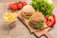 Dois hambúrgueres e batatas fritas com tomates e alface sobre madeira