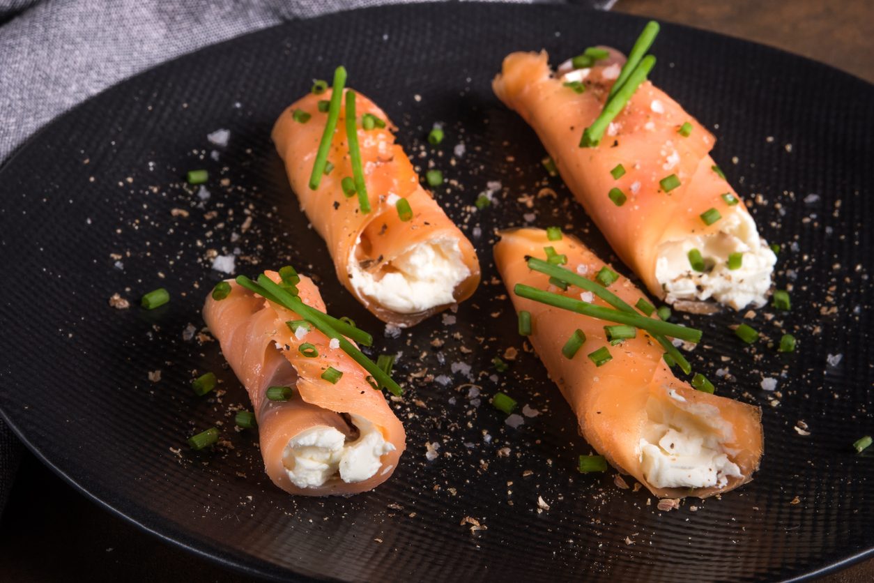 Four salmon rolls on a black plate from a high angle