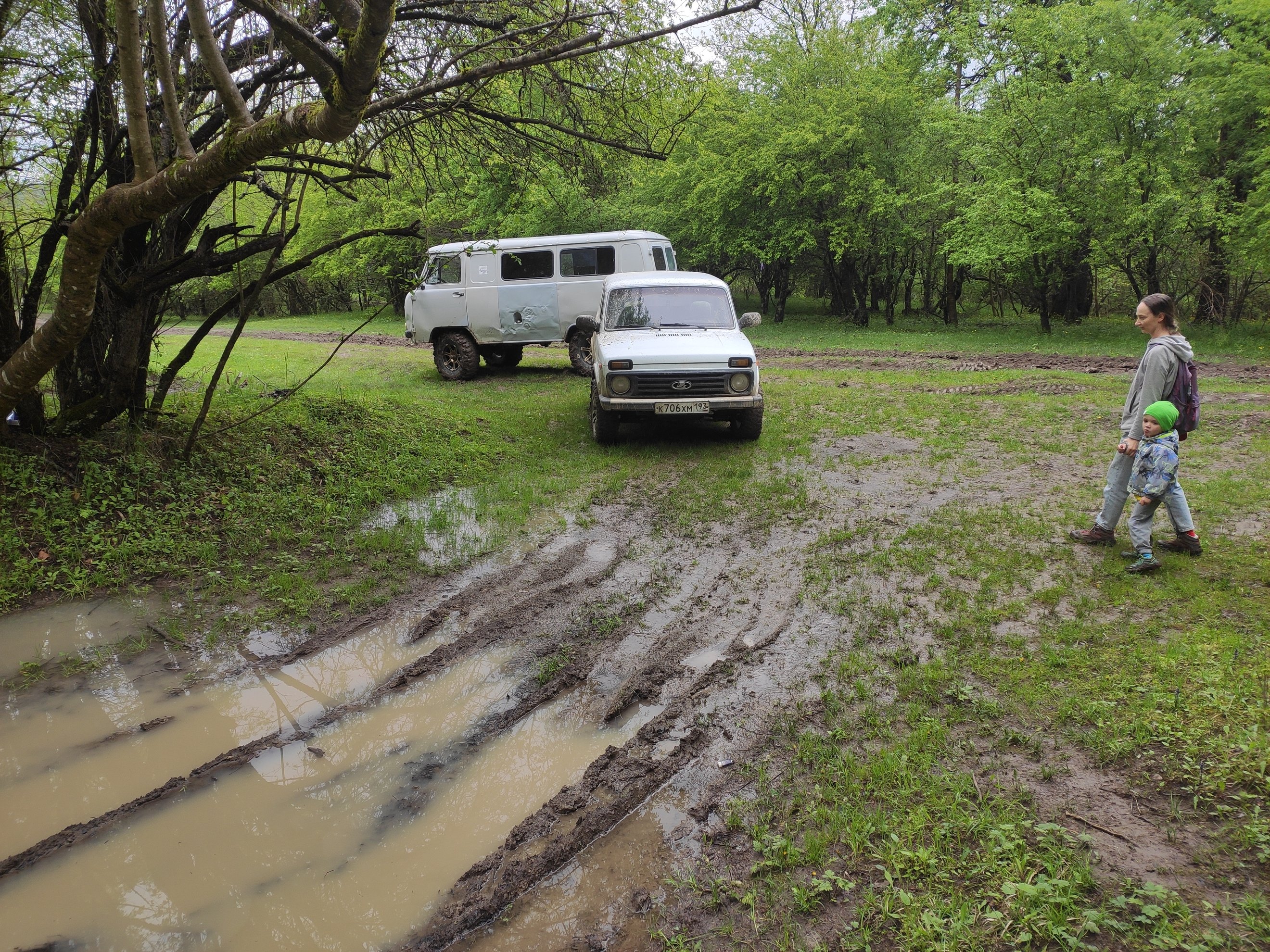 two white vehicles parked on a muddy forest road